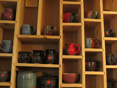 Wooden shelves filled with assorted pottery mugs and jugs.